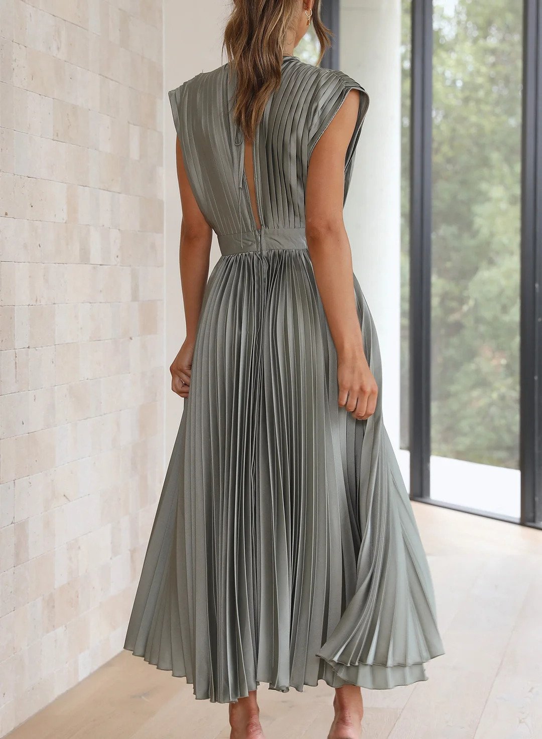 Frau in grauem, plissiertem Midikleid aus Satin, elegantes Design, Rückansicht, Innenraum.