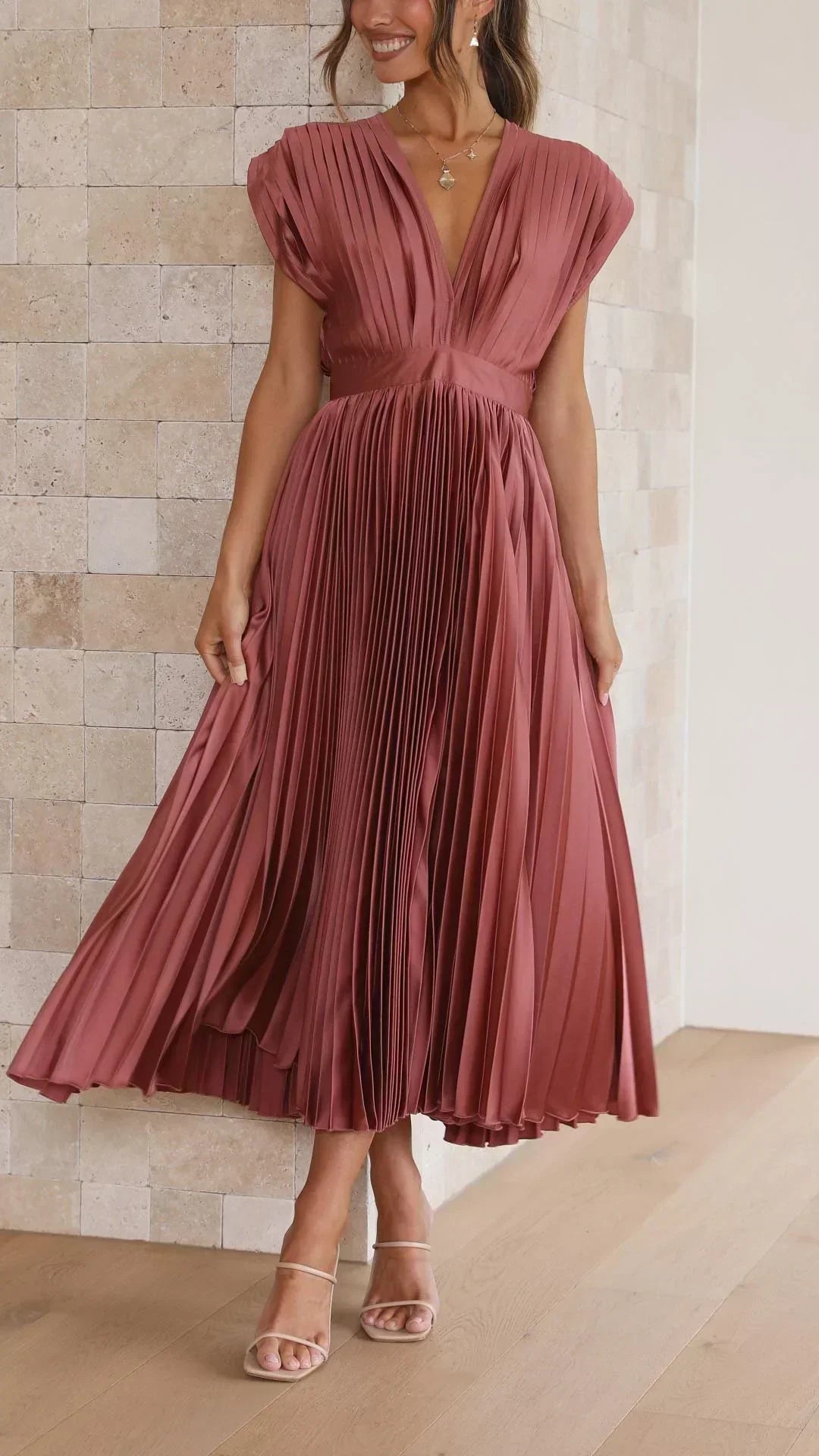 Frau in rotem, plissiertem Maxikleid vor beiger Wand, elegantes Abendmode-Outfit.