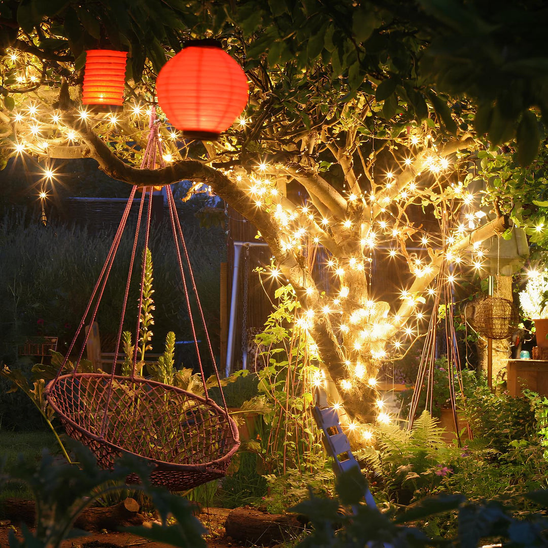 Garten mit Lichterketten, roter Papierlaterne und Hängesessel bei Nacht, stimmungsvolle Beleuchtung.
