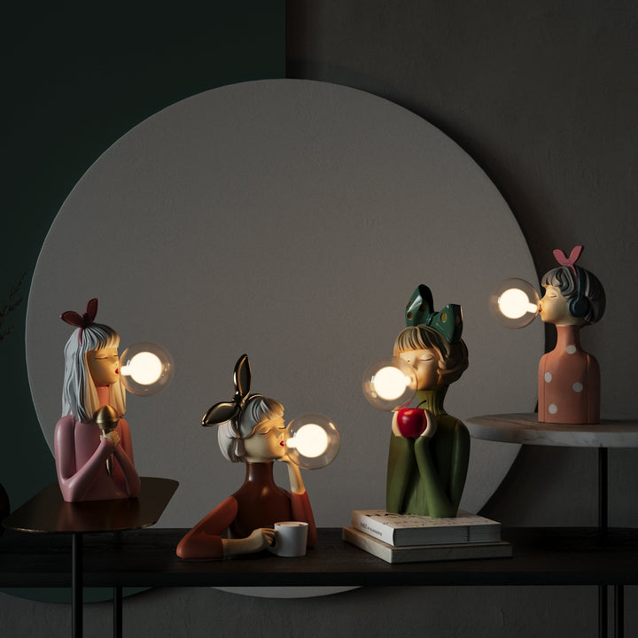 Vier bunte, dekorative Figuren mit Glühbirnen als Kaugummiblasen auf einem Tisch.