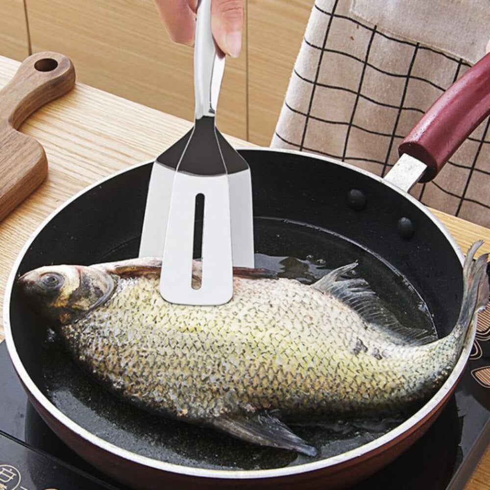 Person brät Fisch in Pfanne mit Edelstahl-Küchenspatel.