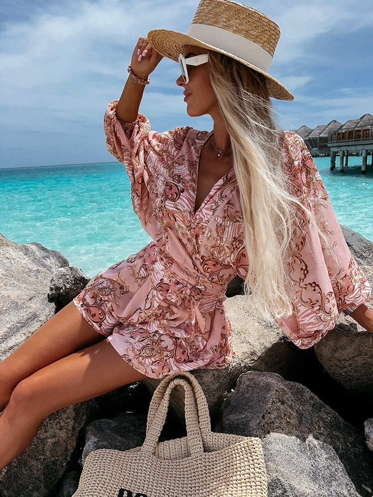 Frau in rosa Sommerkleid und Strohhut am Strand, türkisfarbenes Meer im Hintergrund.