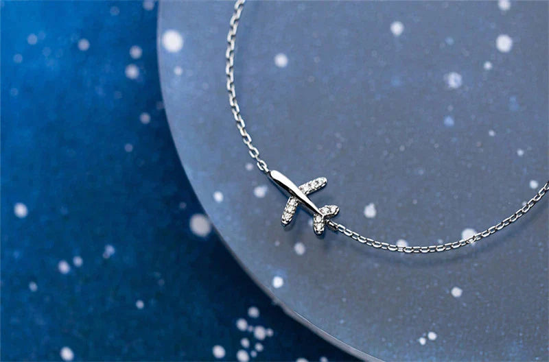 Silberne Flugzeug-Halskette auf blauem Hintergrund, Schmuck, Damenaccessoire, Geschenkidee.