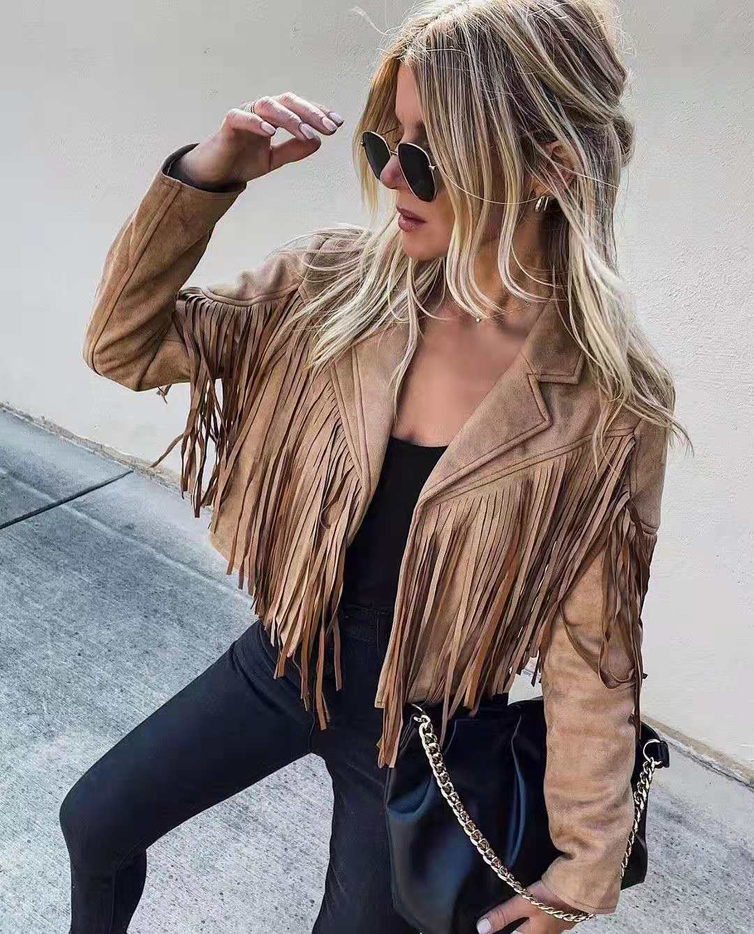 Frau in brauner Wildlederjacke mit Fransen, schwarze Hose, Sonnenbrille, schwarze Tasche.