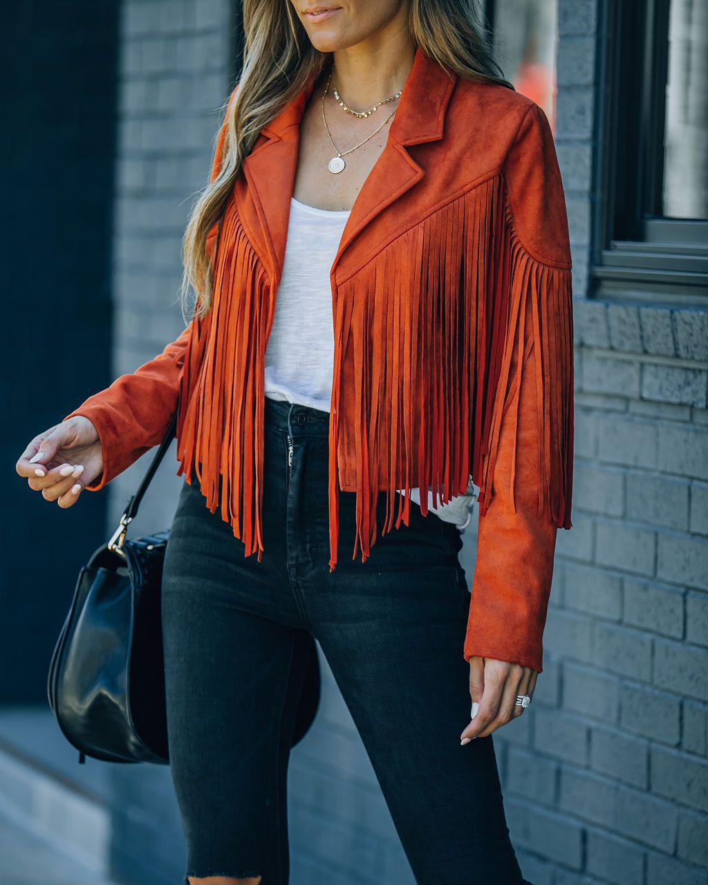 Frau in roter Fransenjacke aus Wildleder, weiße Bluse, schwarze Jeans, modisch, urban.
