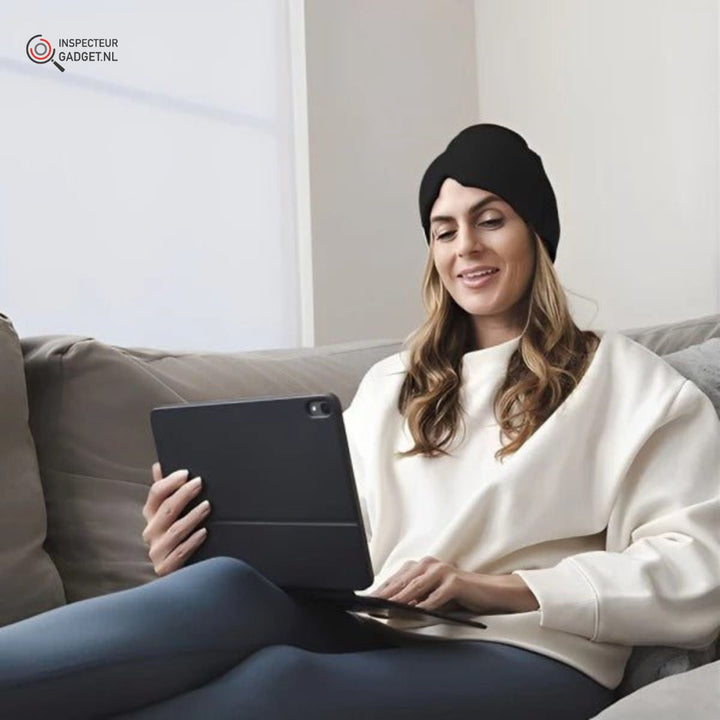 Frau mit schwarzer Mütze und Tablet auf Sofa, gemütlich, moderne Technologie, Innenraum.