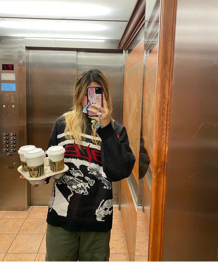 Frau im Aufzug mit schwarzem Pullover, hält vier Kaffeebecher, Selfie im Spiegel.