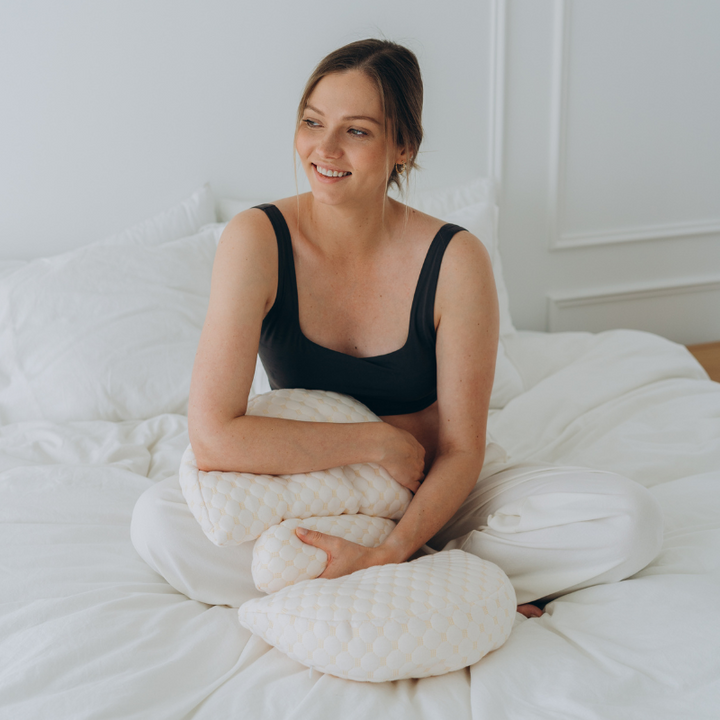 Frau auf Bett mit ergonomischem Stillkissen, weiß, bequem, für Mütter, Stillhilfe, Schlafzimmer.