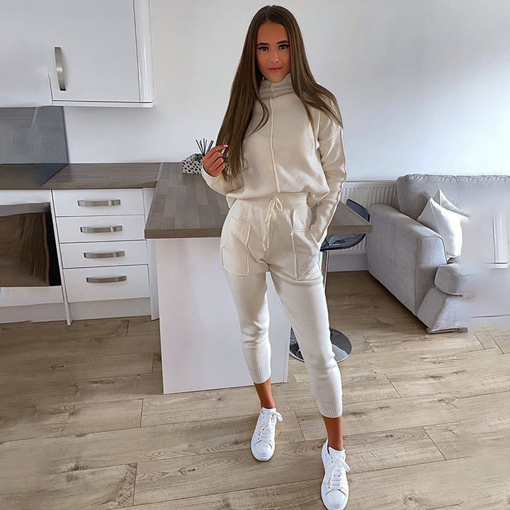 Frau in cremefarbenem Jogginganzug, Kapuzenpullover, Jogginghose, weiße Sneaker, Wohnzimmer.