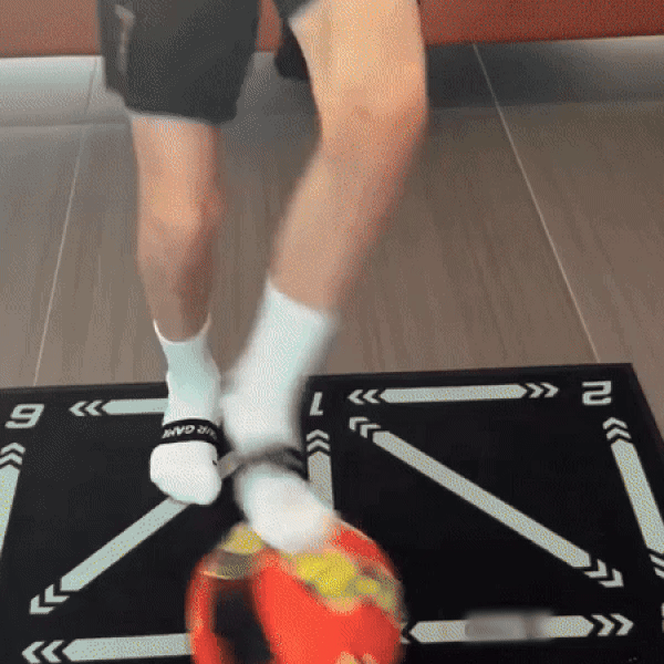 Person jongliert mit rotem Fußball auf schwarzer Matte, trägt weiße Socken und schwarze Shorts.