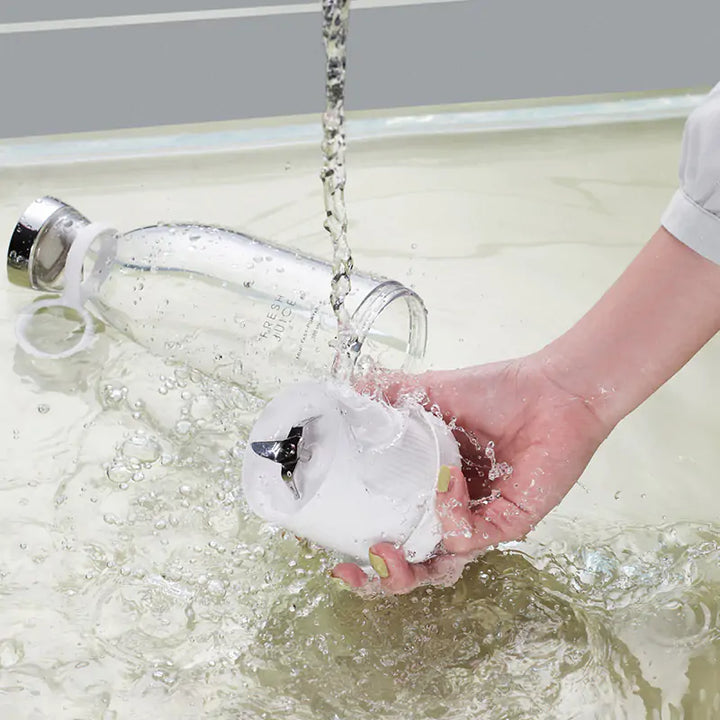 Hand wäscht weißen Mixeraufsatz, Glasflasche im Hintergrund, Wasser fließt, Küchengerät Reinigung.
