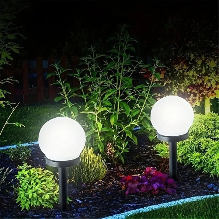 Zwei kugelförmige Solar-Gartenleuchten beleuchten Pflanzen im nächtlichen Garten.