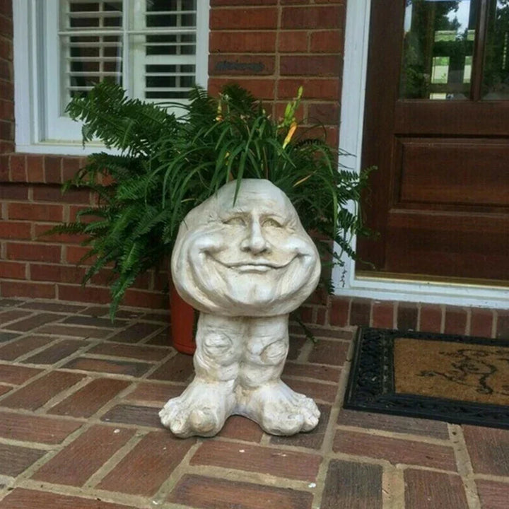 Steinfigur mit Gesicht, lächelnd, auf Terrasse vor roter Ziegelwand, dekorative Gartenstatue.