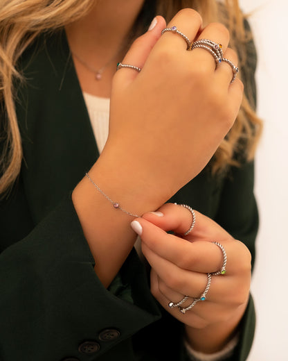 Frau trägt silbernes Armband mit Geburtsstein, mehrere Ringe, eleganter Look, Nahaufnahme.
