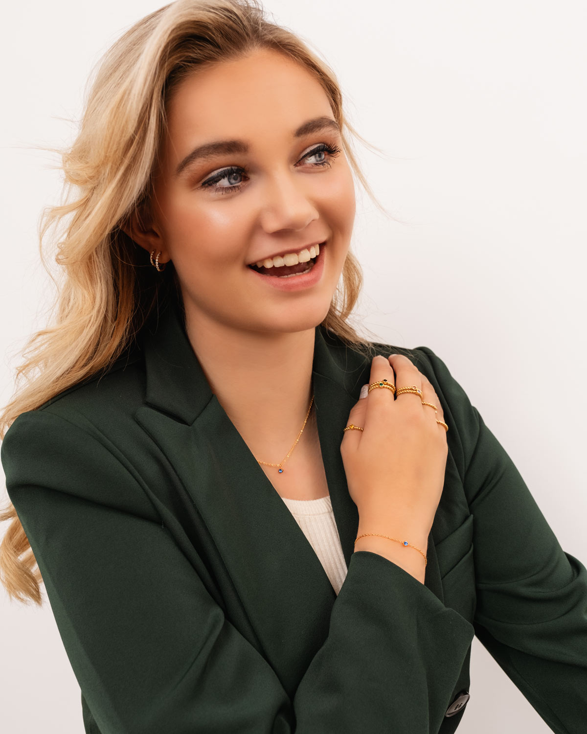 Frau mit goldener Geburtsstein-Kette, grünem Blazer, lächelnd, Schmuckmode.