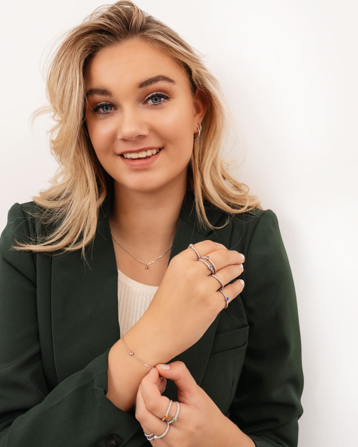 Frau mit grünem Blazer trägt silberne Geburtssteinringe und Armband, lächelnd.
