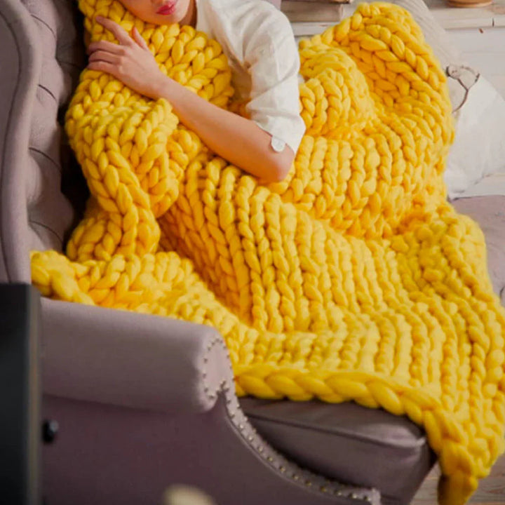 Frau mit gelber, grob gestrickter Decke auf Sofa, gemütlich, Wohnzimmer, Wohnaccessoire.