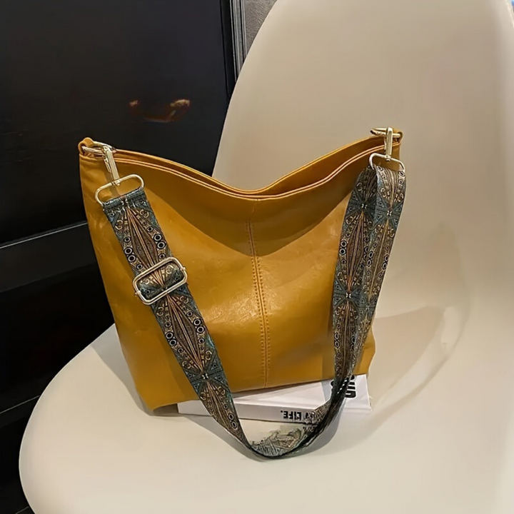 Gelbe Ledertasche mit gemustertem Schultergurt auf weißem Stuhl, modisches Accessoire.