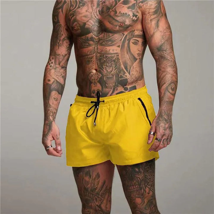Mann mit Tattoos trägt gelbe Badehose, sportlich, Strandmode, Sommerbekleidung, Herrenmode.