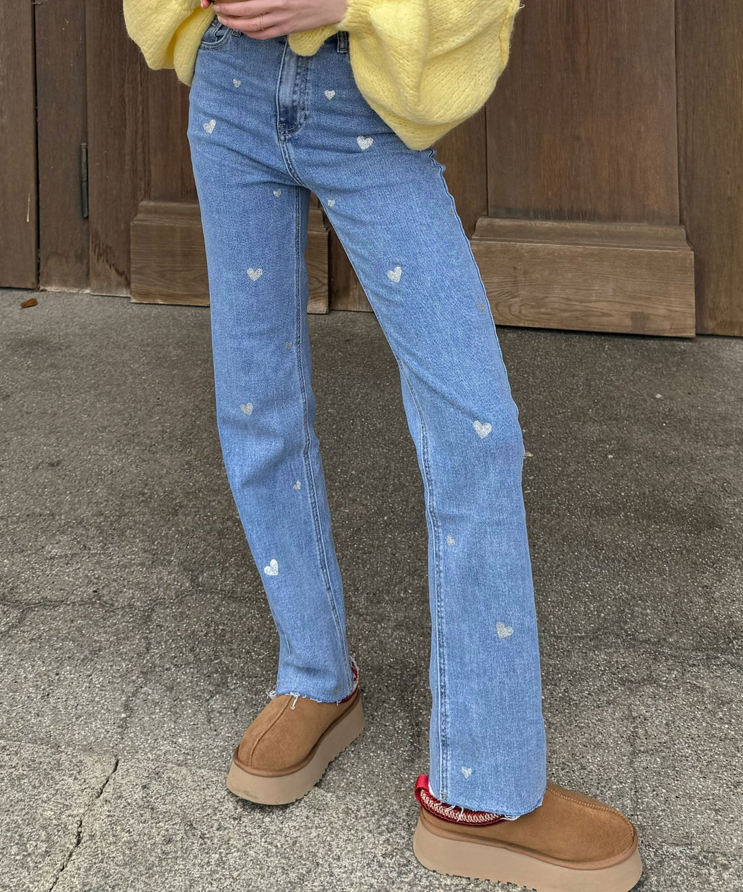 Frau in blauer Jeans mit Herzmuster, gelber Pullover, braune Plateauschuhe, Straße.