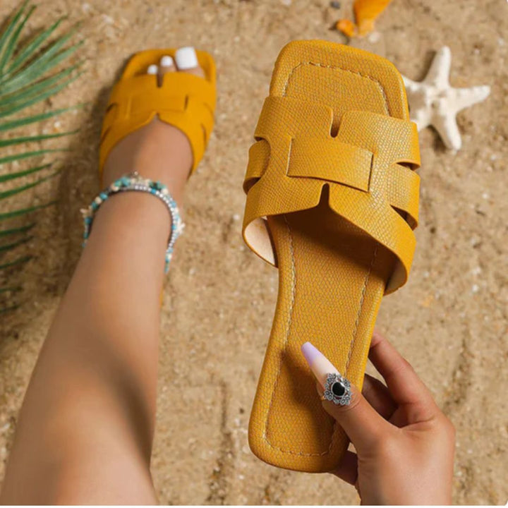 Gelbe Sandale aus Leder auf Sand, Sommermode, Damenfuß, Strandaccessoires, Muschel, Palme.