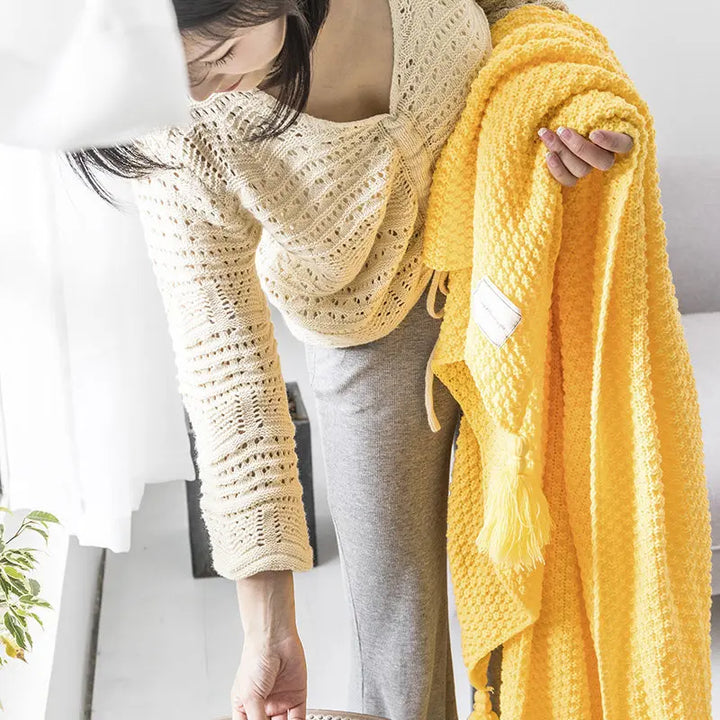 Frau mit gelber Strickdecke, beige Strickpullover, gemütliches Wohnzimmer, skandinavisches Design.