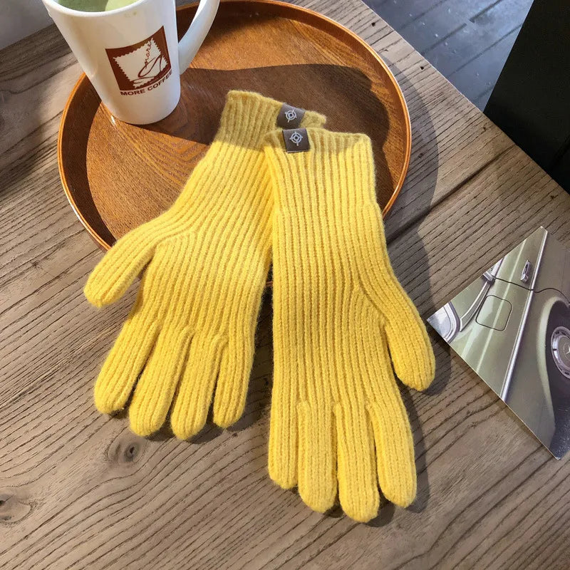 Gelbe Strickhandschuhe aus Wolle auf Holztisch neben Kaffeetasse und Autopostkarte.