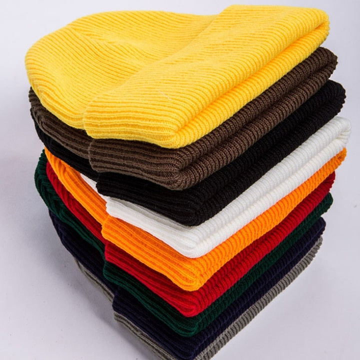 Gestapelte bunte Strickmützen aus Wolle, gelb, braun, weiß, orange, rot, grün, schwarz.