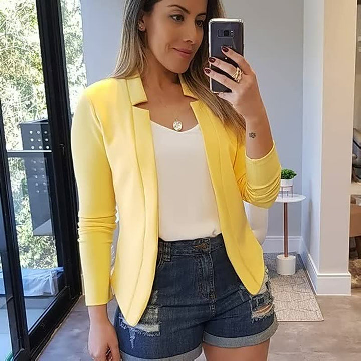 Frau in gelbem Blazer und Jeansshorts, Selfie, modernes Wohnzimmer, modische Freizeitkleidung.