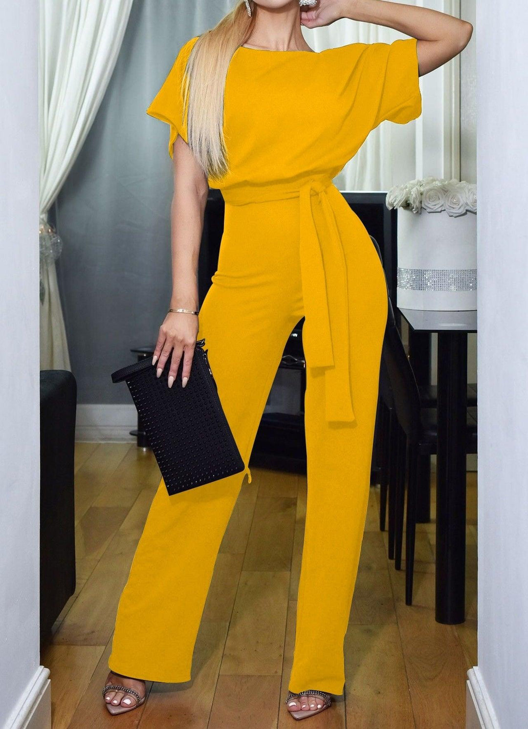 Frau in gelbem Jumpsuit mit schwarzer Clutch, elegantes Abendoutfit, Mode für Damen.