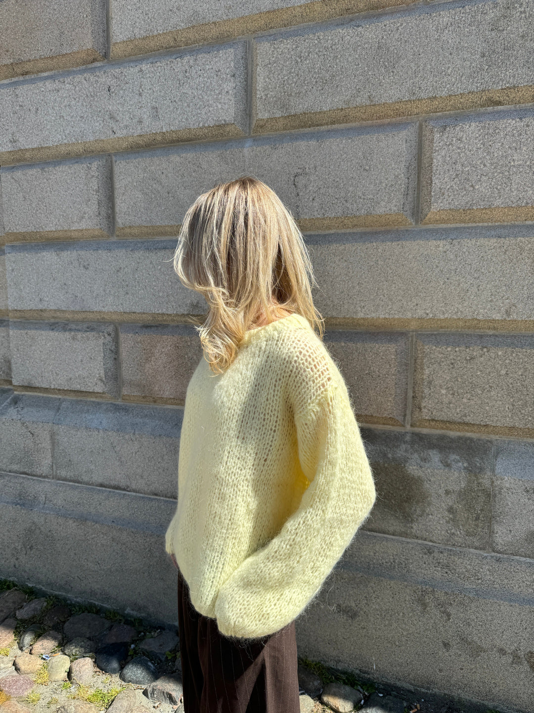 Frau in gelbem Strickpullover vor Steinmauer, modisch, Herbstmode, lässig, warm.