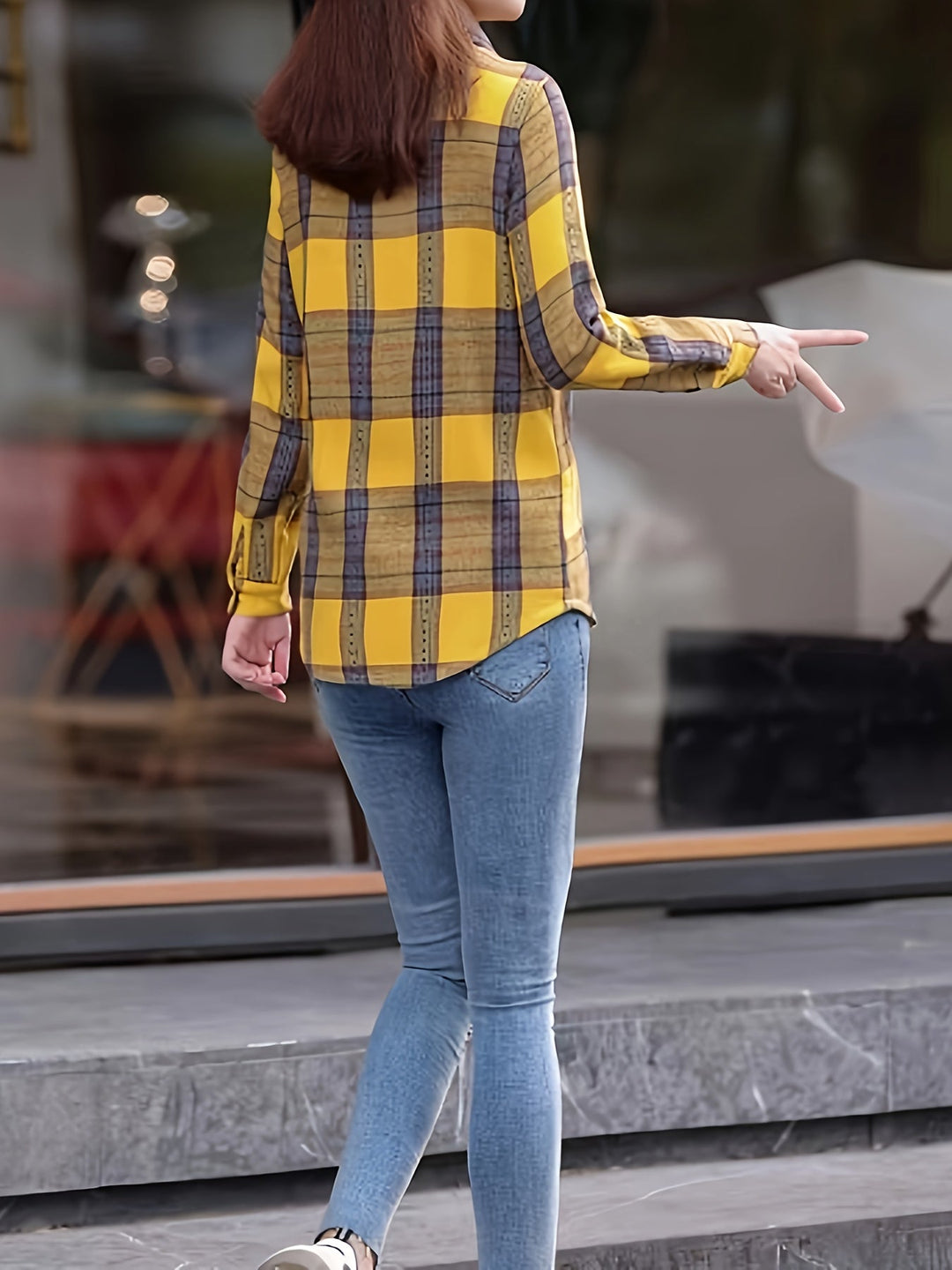 Frau in gelber karierten Bluse und blauer Jeans, geht draußen, Freizeitmode, Rückansicht.