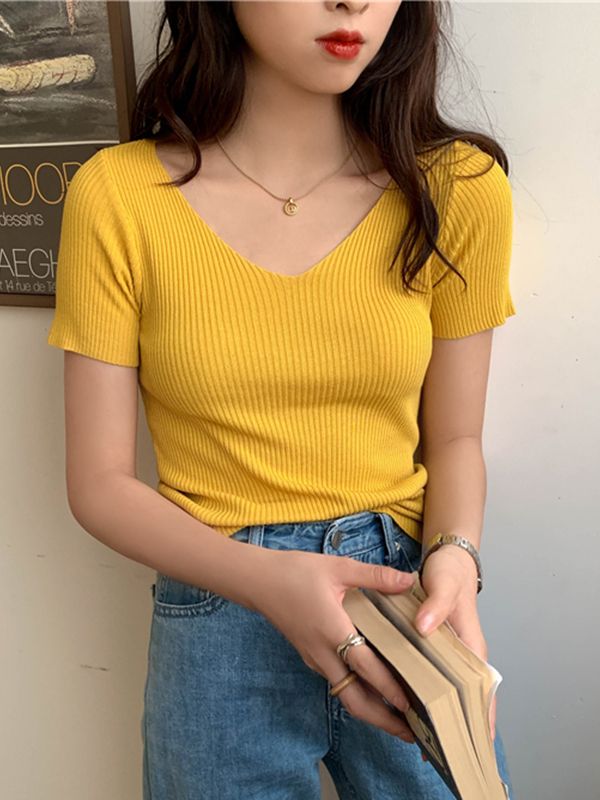 Frau in gelbem, geripptem T-Shirt und blauer Jeans hält ein Buch.