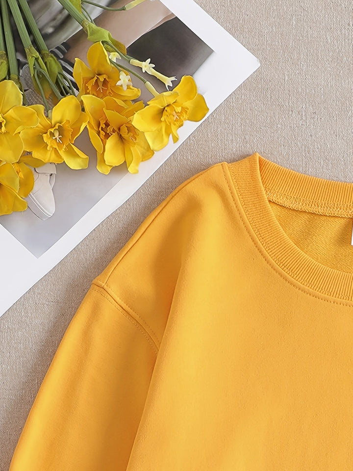 Gelbes Sweatshirt aus Baumwolle neben gelben Blumen auf beigem Hintergrund.