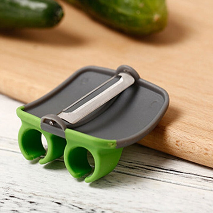 Grüner Gemüseschäler mit Doppelfingergriff auf Holzbrett, ideal für Gurken und Karotten.
