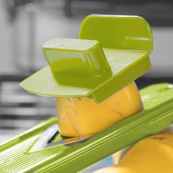 Grüner Gemüsehobel mit gelbem Gemüse, Kunststoff, Küchengerät, sicherer Handschutz.