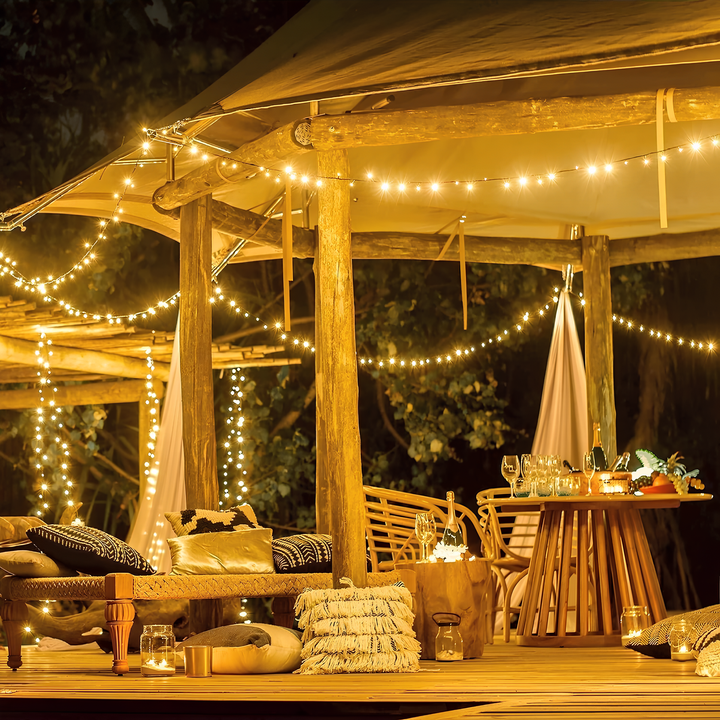 Gemütliche Terrasse mit Holzmöbeln, Lichterketten, Kissen und Tisch, ideal für Abendessen im Freien.