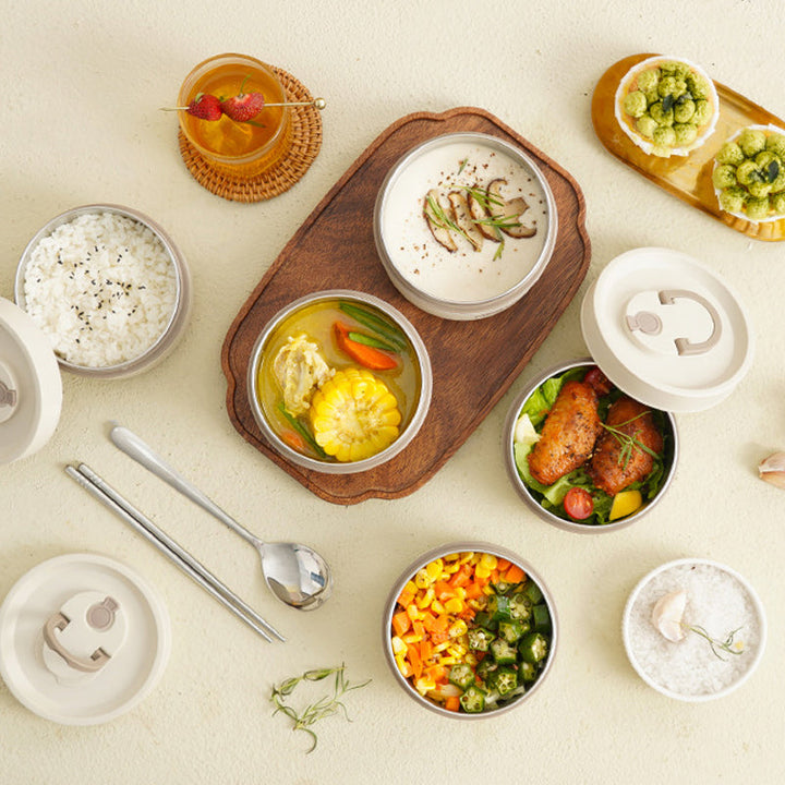 Mehrere Bento-Boxen mit Reis, Gemüse, Suppe und Getränk auf hellem Tisch.