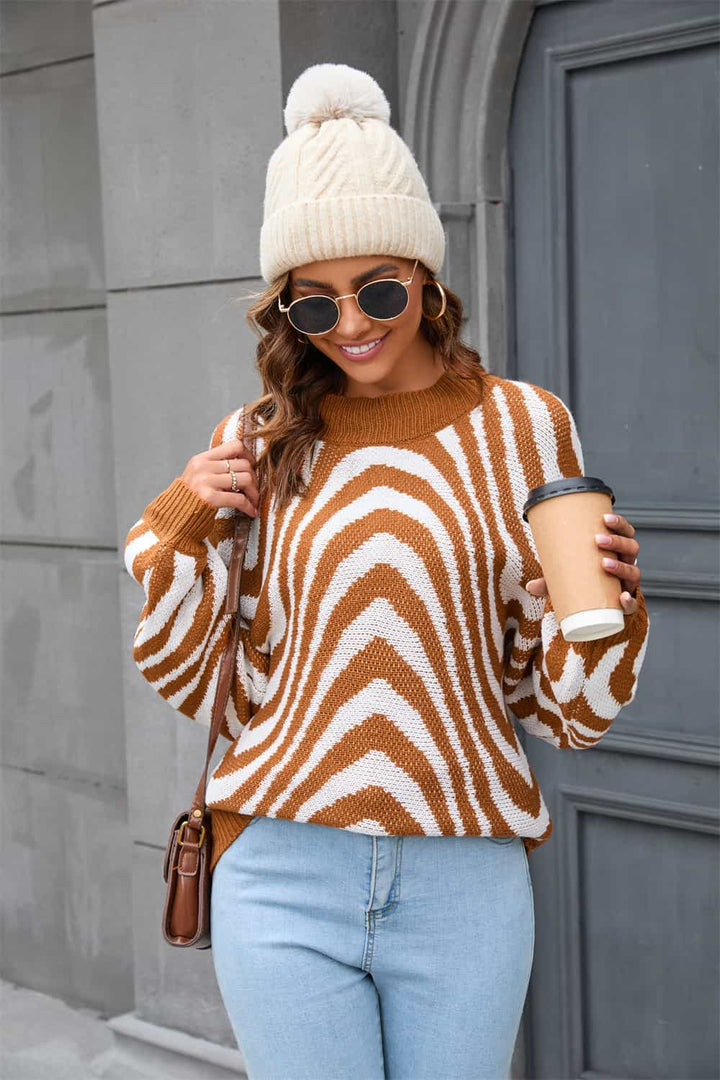 Frau in gestreiftem Pullover, blauer Jeans, weißer Mütze, Sonnenbrille, hält Kaffeebecher.