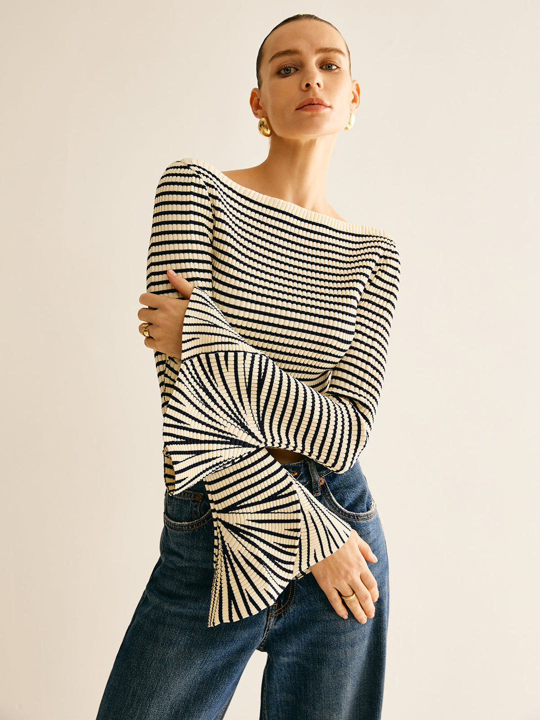 Frau in gestreiftem Pullover mit Trompetenärmeln und blauer Jeans, modisch, elegant.
