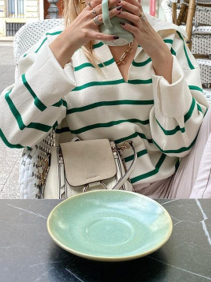 Frau in gestreiftem Pullover trinkt Kaffee, grüne Keramiktasse, modische Handtasche.