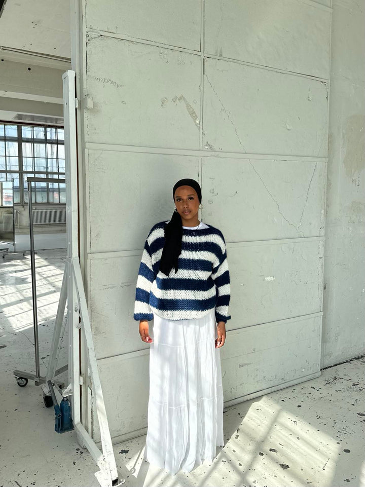 Frau in gestreiftem Pullover und weißem Rock in hellem, industriellem Raum.