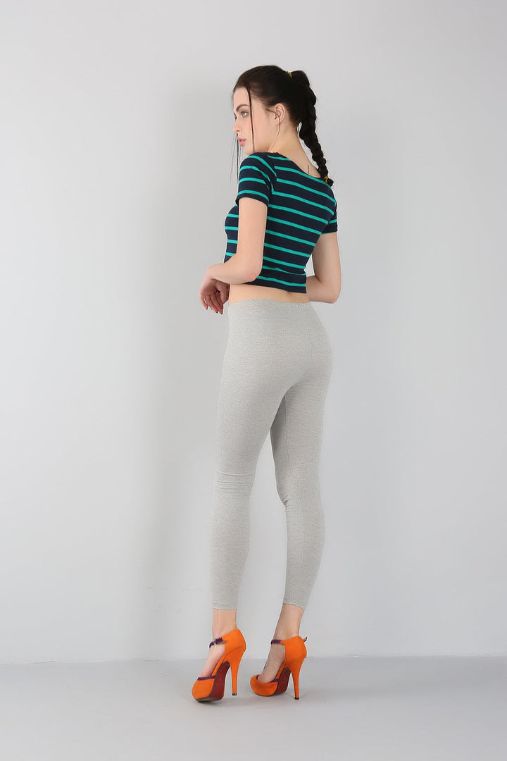 Frau in gestreiftem T-Shirt, grauen Leggings, orangefarbenen High Heels, seitlich stehend.