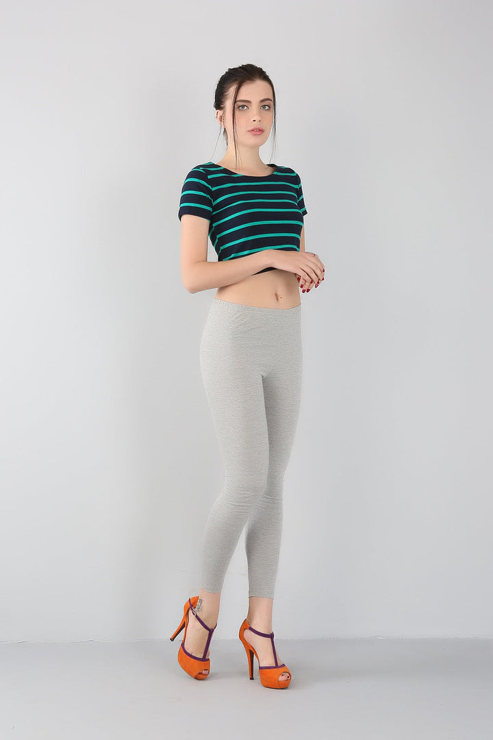 Frau in gestreiftem T-Shirt, grauer Leggings und orangefarbenen High Heels vor grauem Hintergrund.