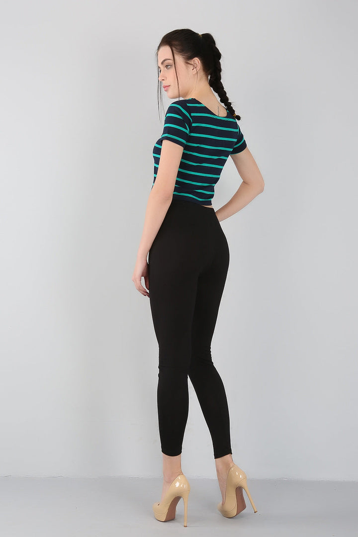 Frau in gestreiftem T-Shirt und schwarzer Leggings, beige High Heels, seitlich stehend.