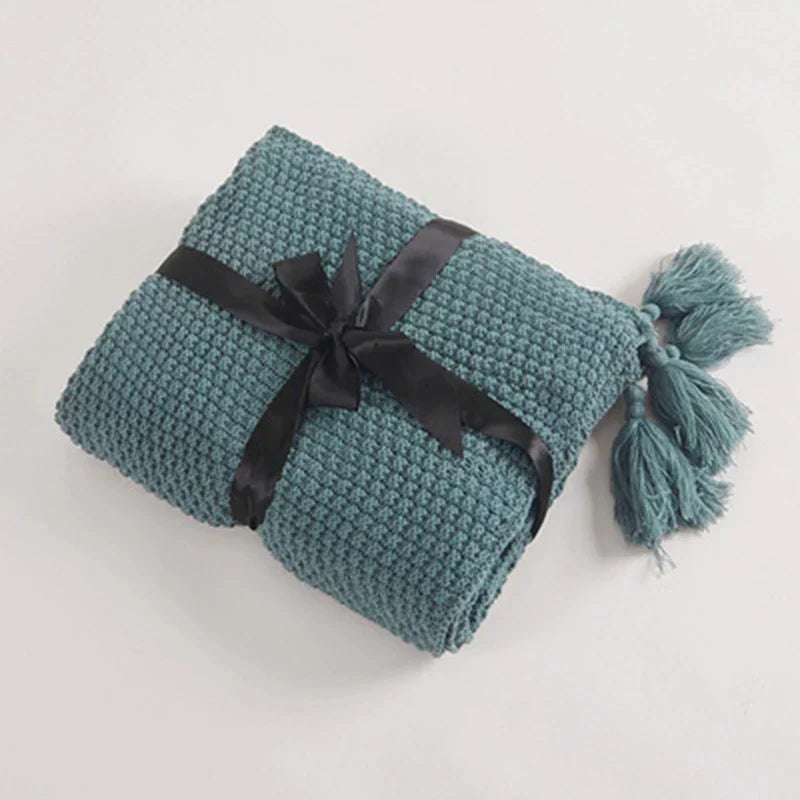 Gefaltete blaue Strickdecke mit schwarzer Schleife und Quasten, gemütliche Wohnaccessoires.