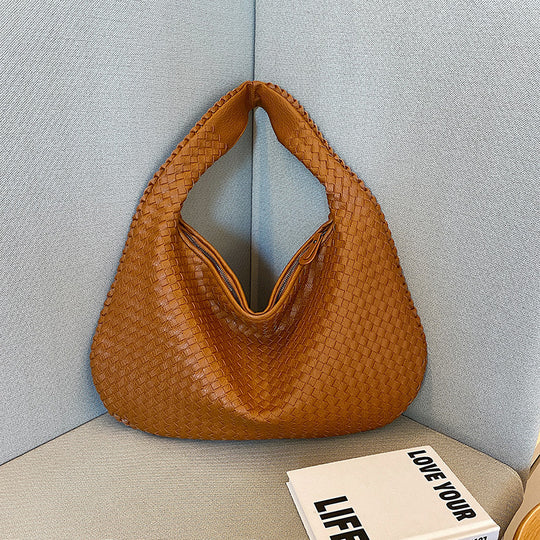 Braune geflochtene Handtasche aus Leder auf grauem Sofa, modisches Accessoire, Damenmode.