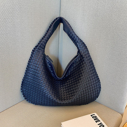Dunkelblaue geflochtene Handtasche aus Leder auf grauem Sofa, modisch, elegant, Damenaccessoire.