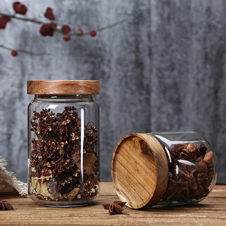 Glasbehälter mit Holzdeckel, gefüllt mit getrockneten Gewürzen, auf rustikalem Holztisch.