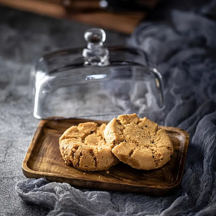Zwei Kekse auf Holztablett unter Glasglocke, rustikaler Hintergrund, Food-Fotografie.